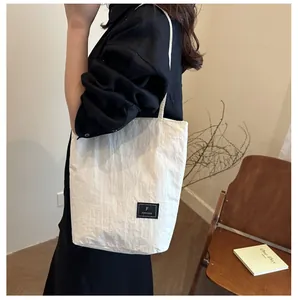 Detailed close-up of white wrinkled nylon tote bag with black logo tag for daily commute