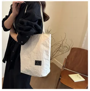 Detail of a creamy white nylon tote bag with unique pleated texture and black woven label