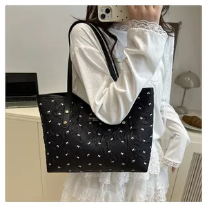 Detail of black quilted tote bag featuring white bow patterns and silver logo plaque