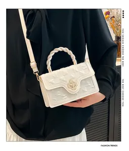 Detail of cream crossbody bag featuring golden flower buckle and woven rope handle