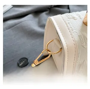 Detailed close-up of white embossed leather handbag showing gold metal hooks and shoulder strap
