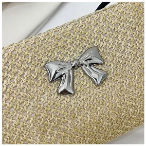Détail du tissage beige avec un nœud décoratif en métal argenté sur un sac d'été