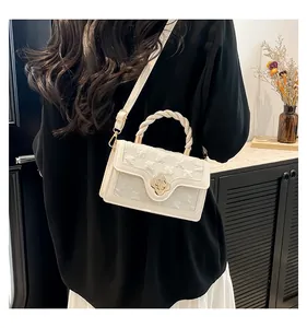 Detail of white embossed crossbody bag with woven handle and gold clover twist lock