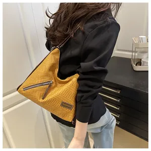 Detalle del bolso tote amarillo con textura de espiga, bolsillo de cremallera y logo