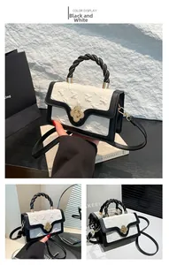 Detail of elegant black and white crossbody bag with gold clover clasp and woven handle