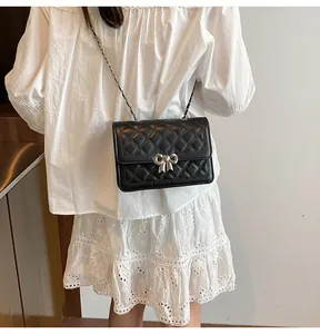 Détail du sac matelassé noir avec fermoir noeud argenté sur robe blanche élégante