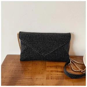 Close-up of a black glitter envelope clutch bag with gold chain strap on wooden surface