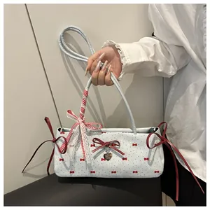 Detail of light blue crossbody bag with red bow prints and a heart-shaped metal pendant