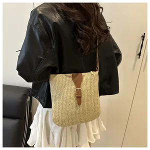 Detailed view of beige woven crossbody straw bag with brown leather strap on model