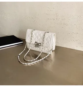 Gros plan d'un sac blanc matelassé avec boucle nœud en métal et bandoulière chaîne sur table
