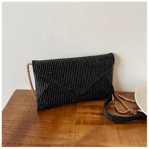 Detail of black rhinestone envelope crossbody bag with a delicate gold chain on wood surface