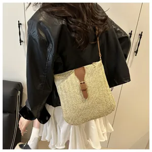 Detail of straw woven crossbody bag with brown leather buckle and slim shoulder strap