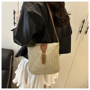 Detail of woven straw crossbody bag with brown leather strap and gold zipper closure