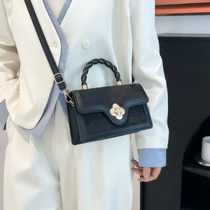 Elegant black crossbody bag with gold floral clasp and woven handle on white suit