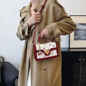 Cute cherry print crossbody bag with woven handle and gold clover clasp on trench coat