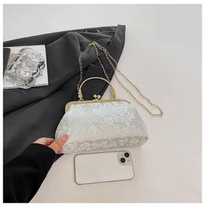 Detail of light cyan brocade handbag with white floral embroidery and gold metal handle