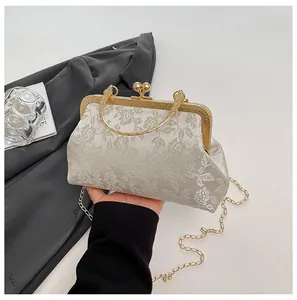 Detail of floral jacquard evening bag with gold metal clasp and top handle held by hand