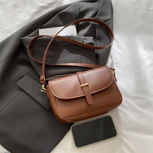 Vintage caramel brown saddle bag with gold buckle and adjustable strap on a gray blazer