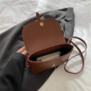 Vintage brown PU leather saddle bag with interior storage space on neutral background