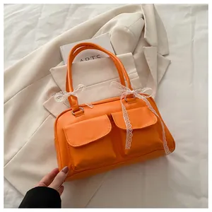 Détail du sac cabas orange vif avec doubles poches avant et accessoire nœud en dentelle blanche