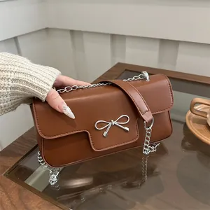 Sac bandoulière marron avec nœud argenté et chaîne posé sur une table en bois élégante