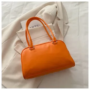 Détail d'un sac bowling en cuir orange vif sur fond texturé avec une veste chic