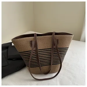Close-up of woven straw tote bag with black stripes and brown leather shoulder straps
