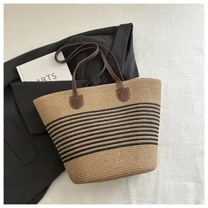 Macro view of woven straw tote bag with black stripes and brown leather handles