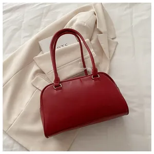 Détail du sac à main rouge en similicuir mat sur un blazer crème aux boucles argentées