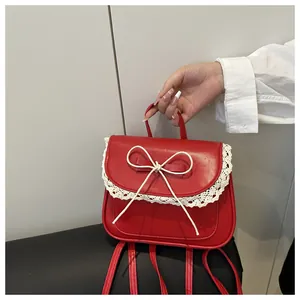 Dettaglio di un piccolo zaino rosso con bordi in pizzo bianco e un fiocco decorativo