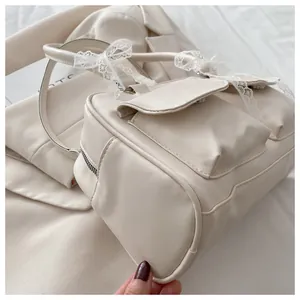 Détail latéral du sac crème montrant le nœud en dentelle et la base en cuir synthétique