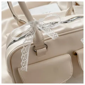 Détail du sac à main crème avec nœud en dentelle délicate et finitions argentées