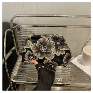 Detailed view of vintage black clutch bag featuring gold floral embroidery and metal chain