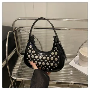 Close-up of black hobo bag with silver rivets on a minimalist shelf background