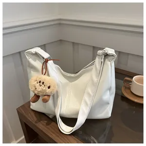 Détail du sac demi-lune blanc avec pendentif chiot en peluche marron sur une table en bois
