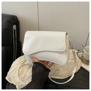 Detail of white glossy patent leather bag with wavy asymmetrical flap and gold hardware