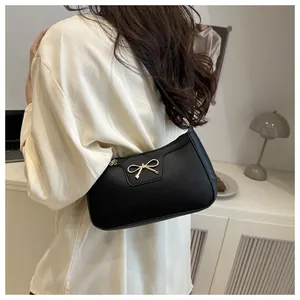 Close-up of black pebble grain hobo bag with gold bow buckle on a casual outfit