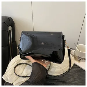 Detailed view of black patent leather shoulder bag with glossy finish and gold metal clasp