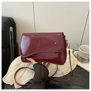 Detail of burgundy patent leather shoulder bag featuring an asymmetrical flap and gold hardware
