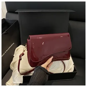Detail of burgundy glossy patent leather bag with gold hardware in luxury gift box