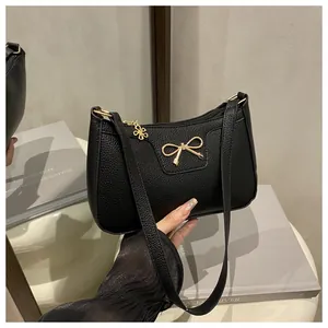 Close-up of black litchi grain leather bag featuring a golden bow and flower charm