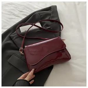 Detail of burgundy patent leather bag with wavy flap design and gold hardware buckle