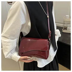 Detail of burgundy glossy patent leather shoulder bag with curved flap and gold metal hardware