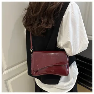Chic burgundy patent leather shoulder bag with asymmetrical flap shown on a model
