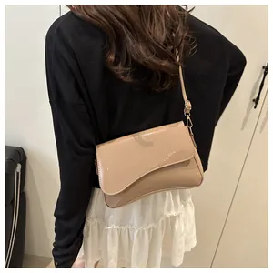 Detail view of khaki patent leather shoulder bag with asymmetrical flap on model
