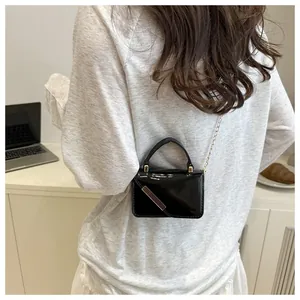 Close-up of mini black patent leather crossbody bag with gold chain and metal detail