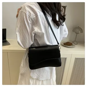 Dettaglio di borsa minimalista in pelle nera con patta a onde e fibbie dorate