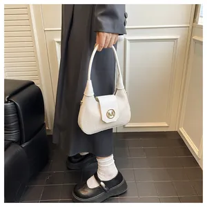 Close-up of a white textured shoulder bag with a gold letter M buckle held by a model