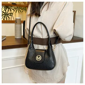 Detail of black woven texture shoulder bag with golden letter M emblem and leather strap