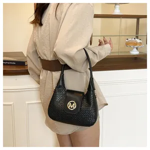 Detail of black woven leather hobo bag with a gold round M buckle in a lifestyle setting
